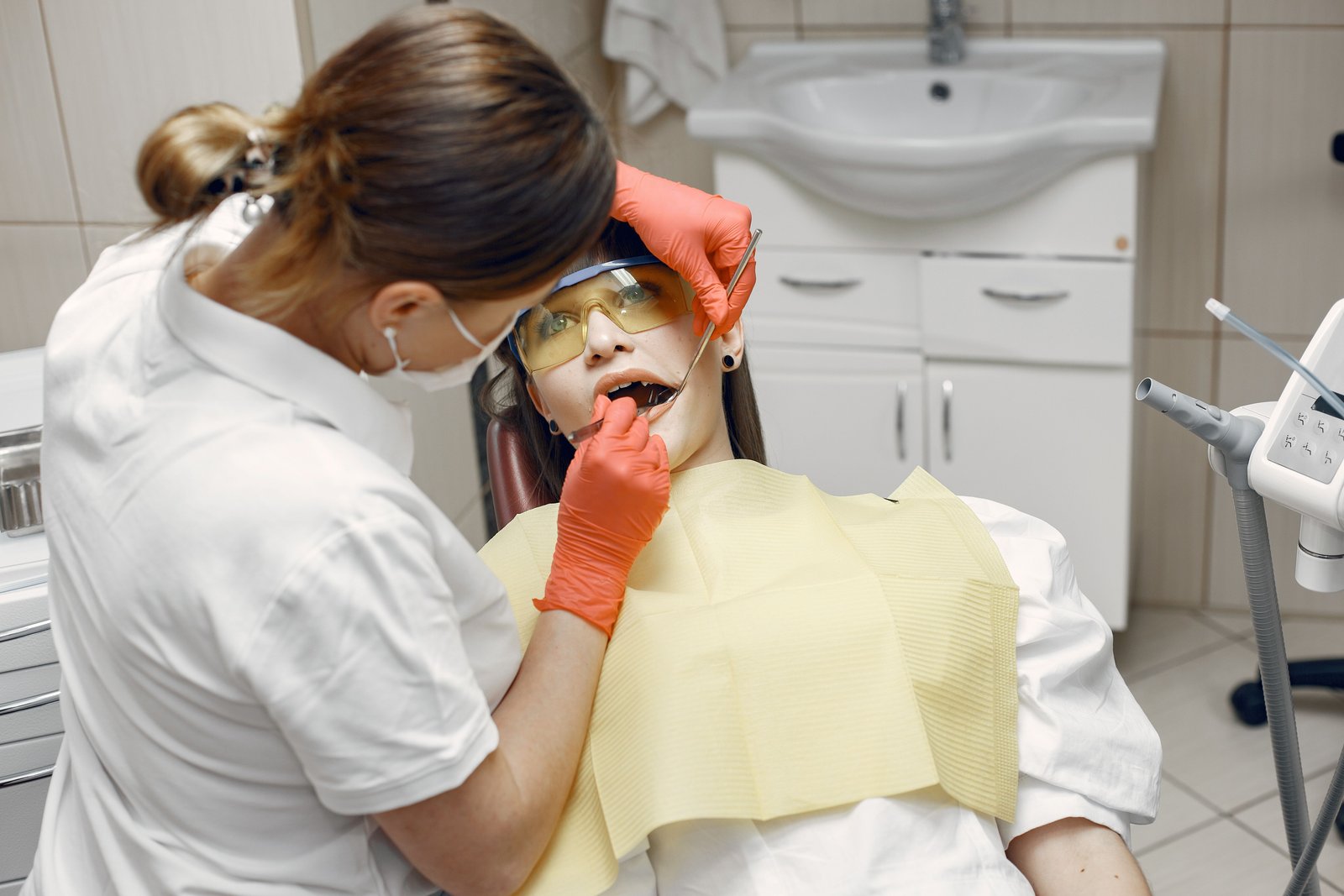 A hygienist in a visor examining a patient's mouth